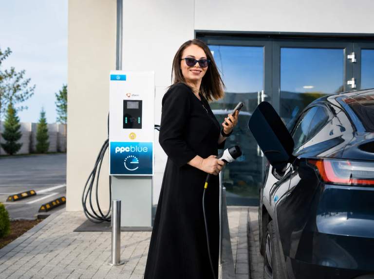 Femeie de afaceri cu telefonul în mână încarcă mașina electrică la stația PPC blue