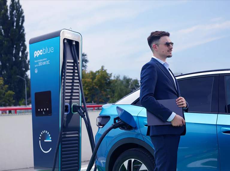 Bărbat în costum lângă mașina electrică conectată la stația de încărcare PPC blue